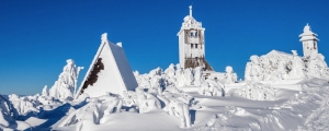 Schneebedeckte Gebäude und Bäume vor klarem blauen Himmel.