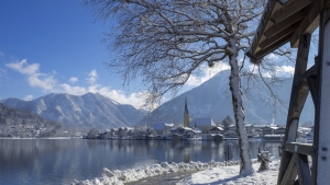 Verschneite Landschaft mit See, Bergen und Dorf im Hintergrund