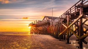 Holzsteg am Strand bei Sonnenuntergang, im Hintergrund leuchtender Himmel.