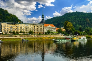 Ein Fluss mit einem Boot, im Hintergrund ein Gebäude und bewaldete Hügel.