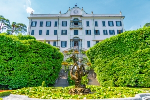 Historisches Gebäude mit Garten und Brunnen im Vordergrund.