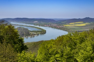 Landschaft mit Fluss und bewaldeten Hügeln unter blauem Himmel.