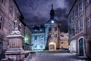 Verschneite Altstadt mit historischem Gebäude und Turmuhr bei Nacht.