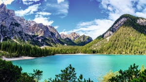 Bergsee mit klarem Wasser, umgeben von Nadelbäumen und Bergen unter blauem Himmel.