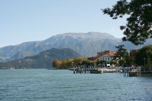 Blick auf den Iseosee mit einer Stadt am Ufer und Bergen im Hintergrund.