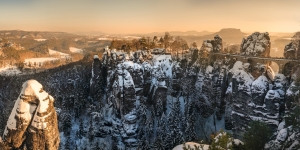 Verschneite Sandsteinfelsen und Brücke im Morgenlicht in einer Berglandschaft.
