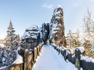 Verschneite Felsenbrücke in winterlicher Landschaft mit verschneiten Bäumen und klarem Himmel.