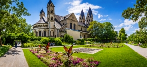 Basilika St. Kastor in Koblenz, umgeben von einem blühenden Garten, mit Bäumen im Hintergrund.