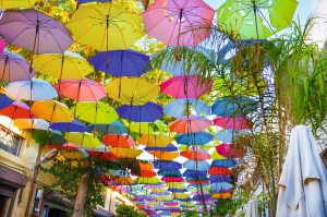 Bunte Regenschirme als Decke über einer Straße mit Bäumen und Gebäuden.