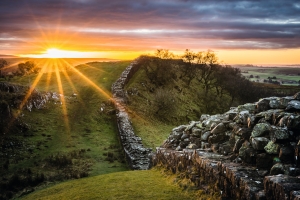 Sonnenaufgang über einer historischen Steinmauer in hügeliger Landschaft.