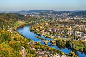 Landschaft mit Fluss, Stadtpanorama und Brücke bei sonnigem Wetter.