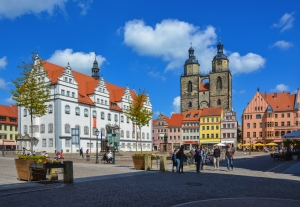 Historischer Marktplatz mit alten Gebäuden und Menschen unter blauem Himmel.