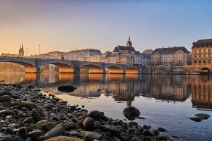 Flusslandschaft mit Brücke und Stadtgebäude im Hintergrund bei Sonnenuntergang.