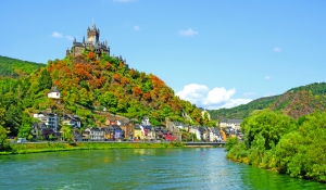Burg auf einem Hügel über einer Stadt am Flussufer bei klarem Himmel.