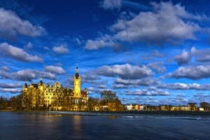 Schloss am See unter bewölktem Himmel bei Sonnenschein.