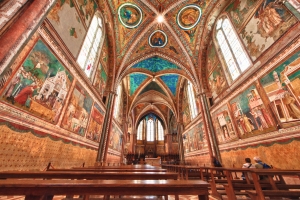 Innenansicht einer reich verzierten Kirche mit Fresken und Bänken.