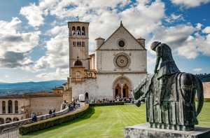 Kirche mit Glockenturm und Reiterstatue im Vordergrund bei blauem Himmel.