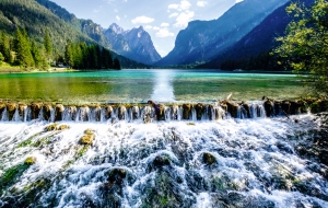 Bergsee-Landschaft mit Wasserfall, umgeben von Wäldern und Bergen.