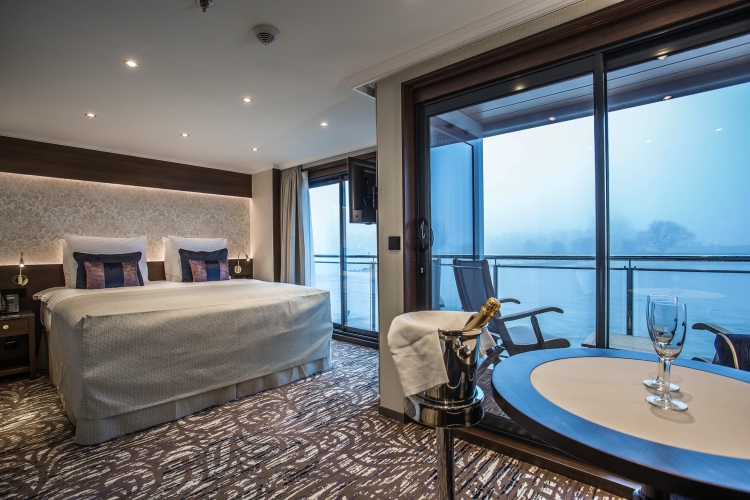 Luxuriöse Suite mit Doppelbett und Balkon, Blick auf neblige Landschaft, Champagner auf Tisch.