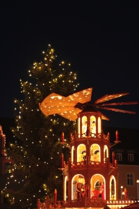 Weihnachtspyramide und beleuchteter Baum vor Nachthimmel.