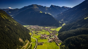 Luftaufnahme eines Tals mit Dorf, umgeben von bewaldeten Bergen.