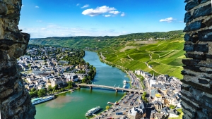 Ausblick auf Fluss und Stadt mit Brücke, umgeben von grünen Hügeln und Weinbergen.