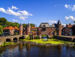 Historische Stadtmauer mit Türmen und Brücke an einem sonnigen Tag.