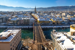 Stadtansicht im Winter mit Kirche, Fluss und schneebedeckten Häusern, Brücke im Vordergrund.