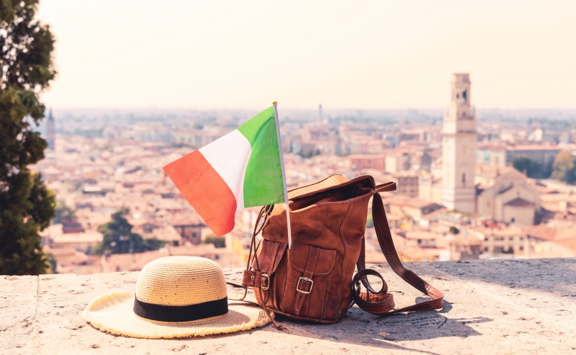 Hut, Rucksack und italienische Flagge vor Stadtpanorama.