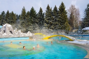 Aussicht auf die Johannesbad Therme im Winter mit Menschen im dampfenden Außenbecken.