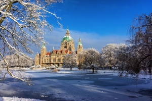 Neues Rathaus Hannover im Winter, umgeben von schneebedeckten Bäumen und zugefrorenem Teich.