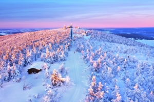 Schnee bedeckte Landschaft mit Hügeln und Wald im Abendlicht.