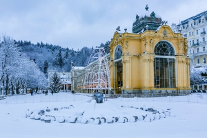 Kolonnade in Marienbad im Schnee, umgeben von Winterlandschaft und verschneiten Bäumen.