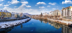 Stadtfluss im Winter mit Schnee und Häusern, klarer Himmel mit Wolken.