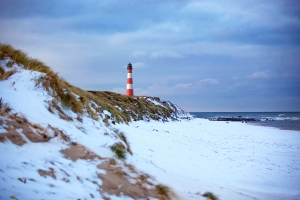 Leuchtturm auf schneebedeckter Dünenlandschaft am Meer unter bewölktem Himmel