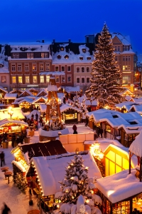 Verschneiter Weihnachtsmarkt bei Abenddämmerung mit festlich beleuchteten Ständen.