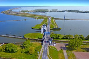 Luftaufnahme einer Schleuse und Brücke in einer flachen Wasserlandschaft.