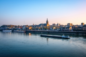 Stadtansicht mit Fluss, Kirchturm und Schiff im Vordergrund bei Sonnenaufgang.