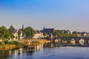 Historische Stadtansicht mit Fluss und Brücke bei klarem Himmel.