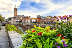 Blumen im Vordergrund, Kanal mit Brücke und Kirchturm im Hintergrund.