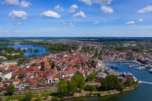 Luftaufnahme einer Stadt mit Hafen, rotem Ziegeldach und umgebender Landschaft.