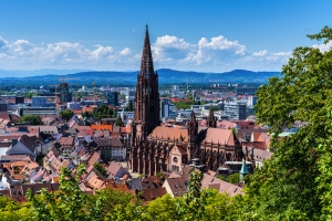 Panorama von Freiburg mit dem Münster im Zentrum und Bergen im Hintergrund.