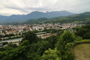 Panoramablick auf eine Stadt mit Bergen im Hintergrund und einem Fluss im Vordergrund.
