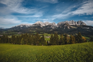 Panorama des Wilden Kaisers im Herbst, grüne Wiesen und bewaldete Berge im Hintergrund.