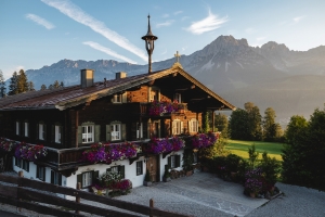 Traditionelles Holzhaus mit Blumen vor Bergkulisse bei Sonnenschein.
