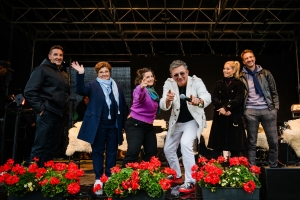 Sechs Personen auf einer Bühne mit Blumen im Vordergrund.