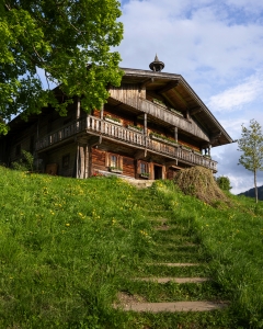 Holzhaus im Grünen mit überdachten Balkonen und blühender Wiese im Sommer.