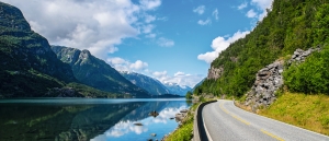 Straße entlang eines Fjords in Norwegen mit Bergen und blauen Himmel.