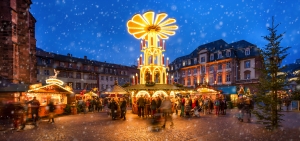 Weihnachtsmarkt mit beleuchteter Pyramide und schneebedeckten Ständen bei Abenddämmerung.