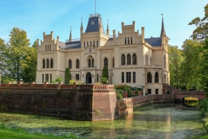 Historisches Schloss mit Wassergraben im Park, umgeben von Bäumen.